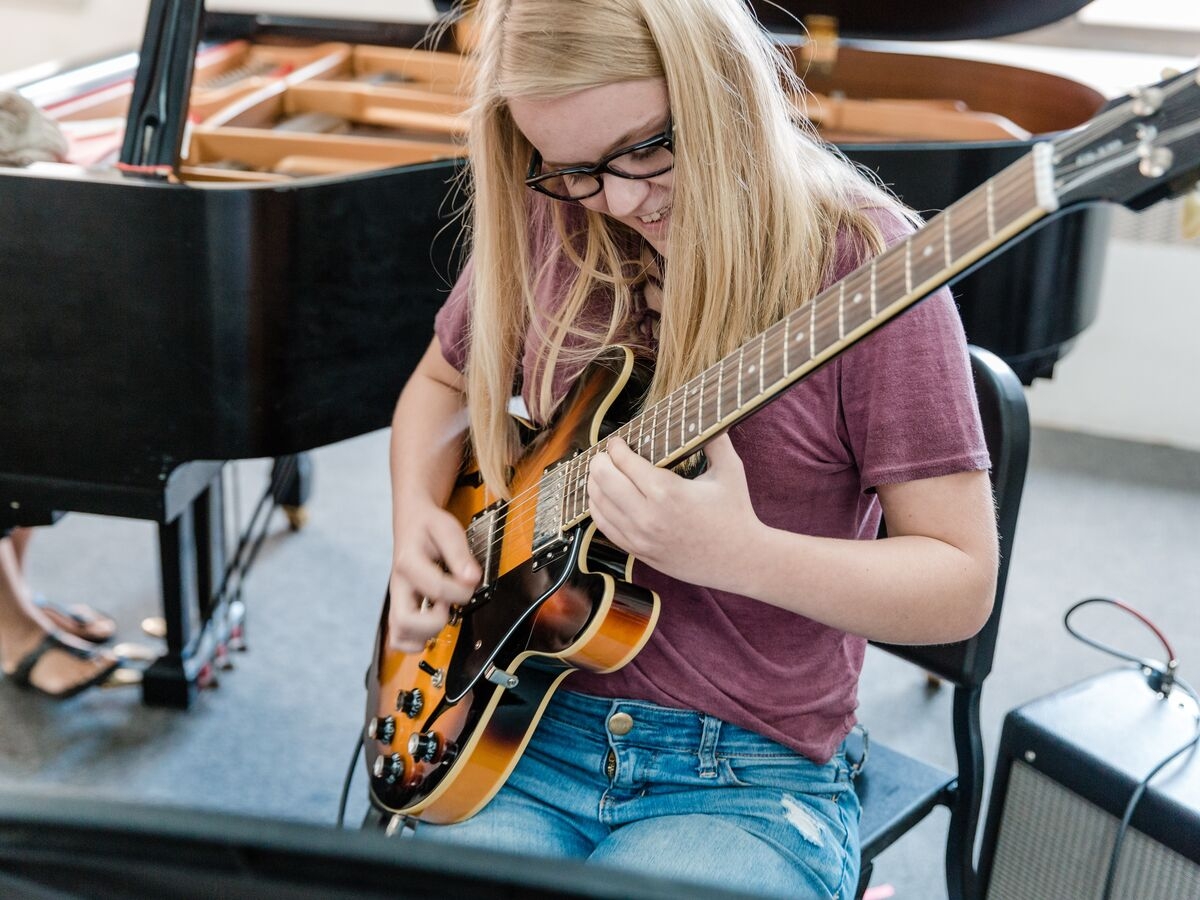 A guitarist rehearses in front of a piano