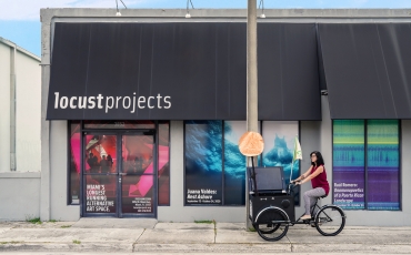Woman riding a tricyle on the sidewalk outside of a Miami art gallery