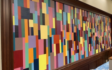 An abstract indoor mural comprising multicolored squares and rectangles of differing sizes, on a wood wall