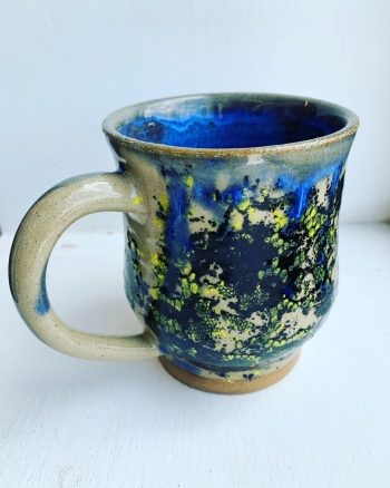 A mug painted abstractedly in blue and green and yellow and tan