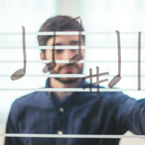 In the foreground drawn music notes, through a clear whiteboard a man in the background draws the notes.