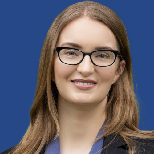 Dr. Emily Mattingly smiling and wearing glasses in front of a blue background.
