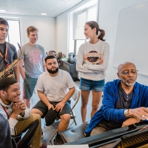 Music students gather around their instructor at the piano