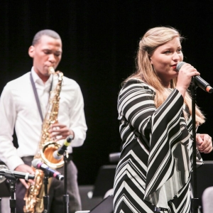 A vocalist and saxophone player perform on stage