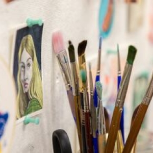 close-up of brushes in a container standing upright in a studio nook, with pinned images on the wall 