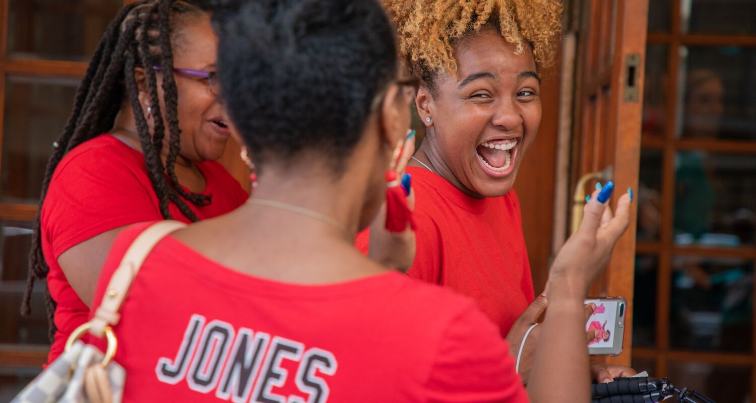 three students in red T-shirts; one student is facing the camera and laughing.