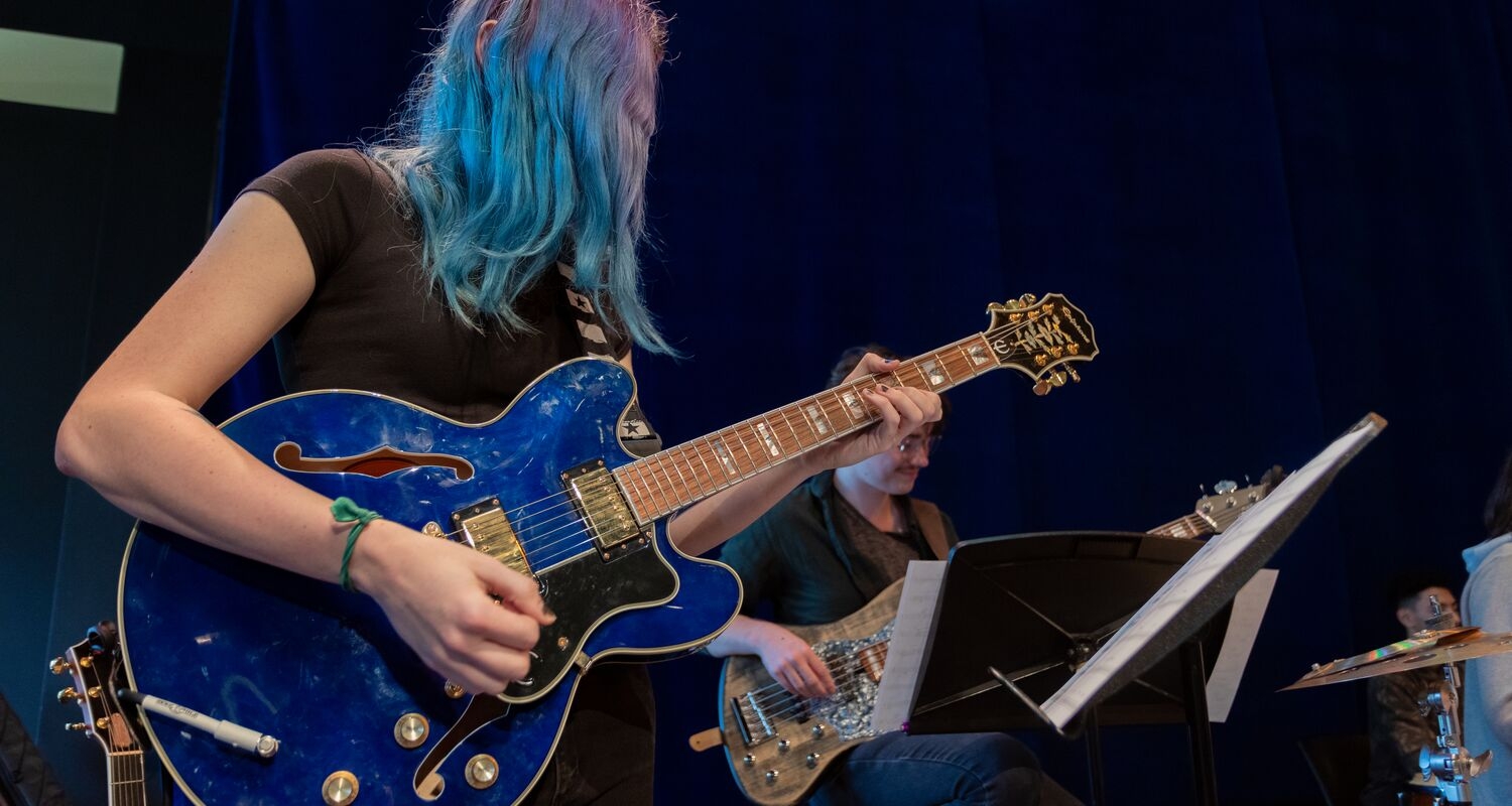 UArts student playing a blue guitar in an ensemble 