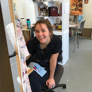 A student smiles at the camera while working on their art in the painting studios.